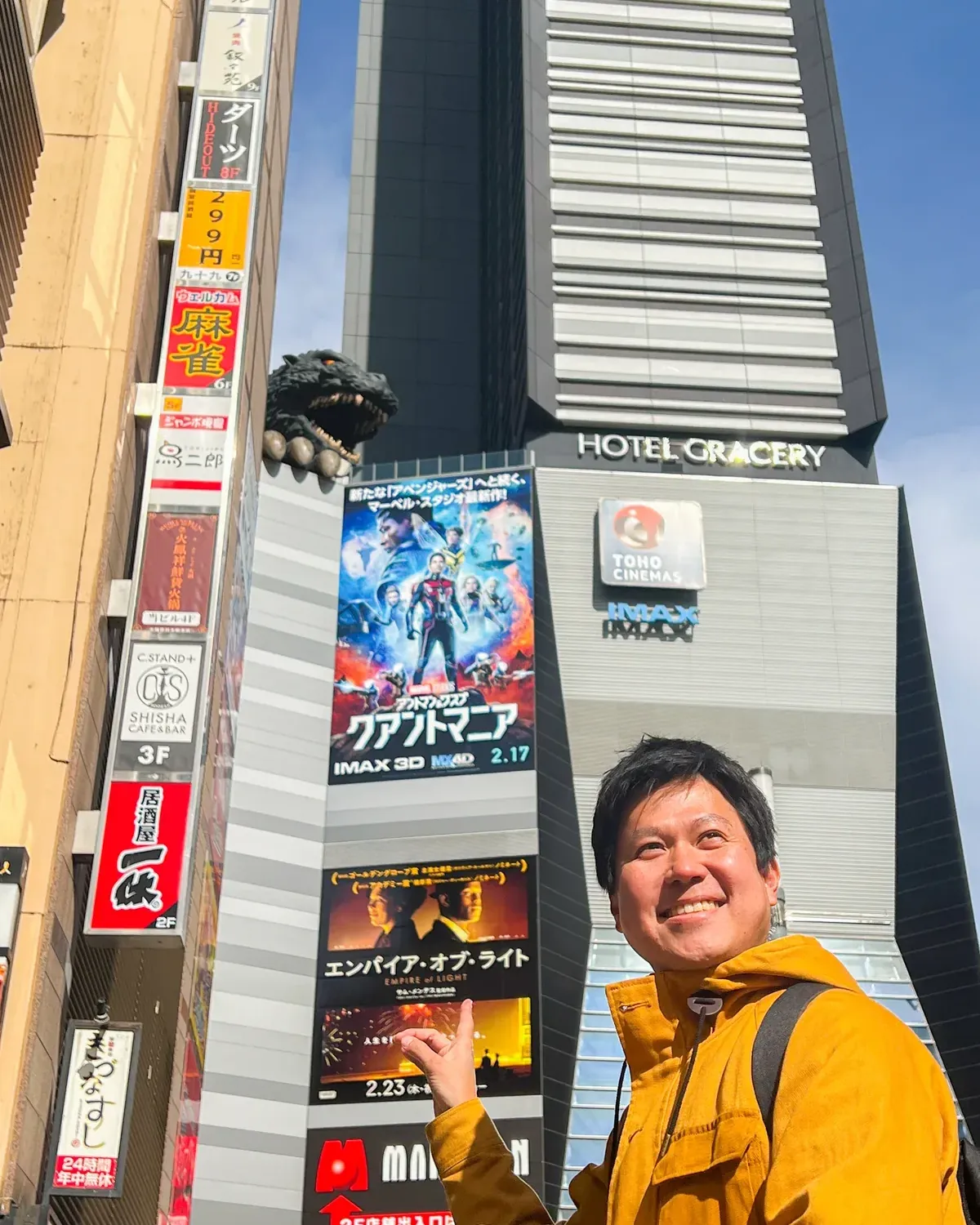 A guide and a guest pointing up at the Godzilla head on the Toho building in Kabukicho