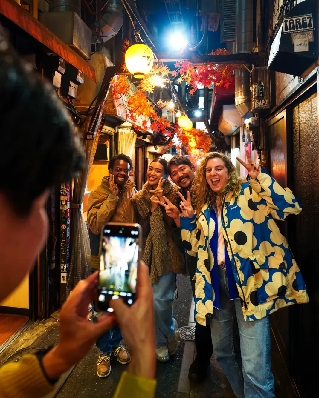 Guests taking photos under the lanterns in an Omoide Yokocho alley at night